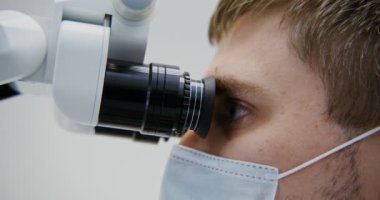 Erkek dişçi diş mikroskobuyla hastaların diş köklerine bakar.