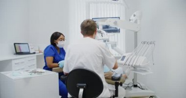 Erkek dişçi diş mikroskobuyla hastaların diş köklerine bakar.