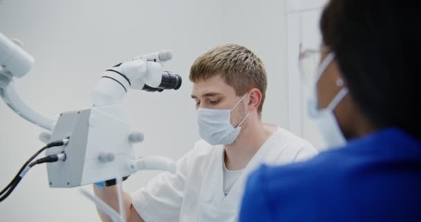 Dokter gigi laki-laki melihat melalui mikroskop gigi untuk pasien gigi saluran akar — Stok Video