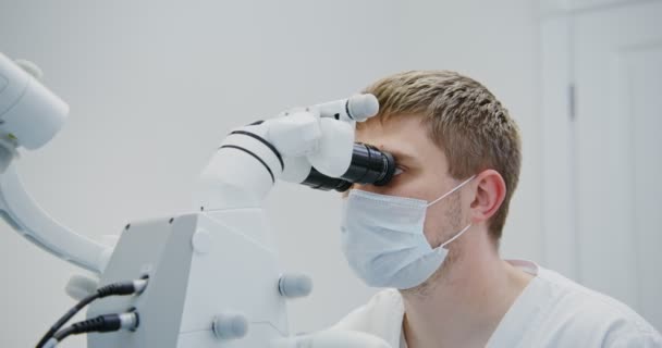 Homme dentiste regarde à travers le microscope dentaire pour les patients canal radiculaire dentaire — Video