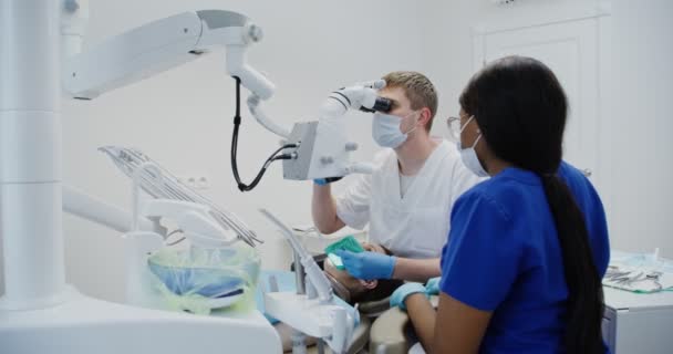 Odontólogo masculino mira a través del microscopio dental para pacientes canal de la raíz dental — Vídeos de Stock