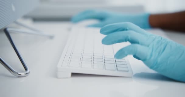 Un médico con guantes azules desechables está escribiendo en un teclado de computadora — Vídeo de stock