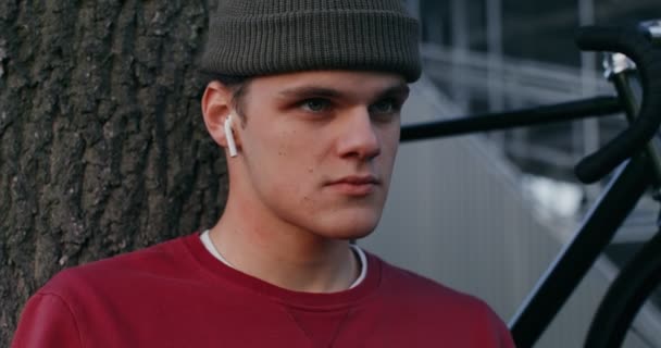 Seorang pemuda memasukkan headphone nirkabel ke telinganya, mulai mendengarkan — Stok Video
