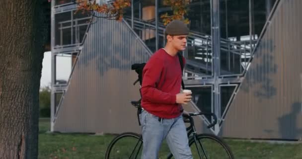 Un jeune homme marche à travers la ville d'automne, conduisant un vélo dans ses mains — Video