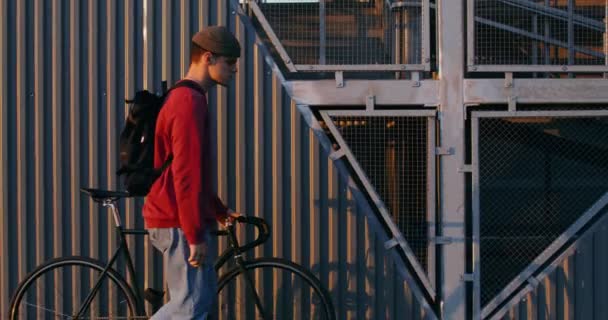 Een jongeman leidt een fiets in zijn handen, die door de stad rijdt — Stockvideo