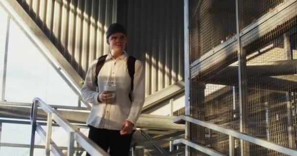 Un jeune homme descend un escalier en métal, tenant une tasse de café — Video