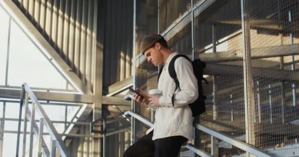 Un jeune homme utilise un téléphone portable et boit du café, gros plan — Video