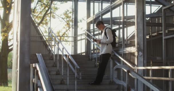 Un homme utilise un téléphone portable et boit du café debout sur un escalier en métal — Video