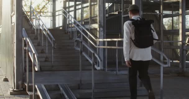 Sırtında sırt çantası olan genç bir adam metal merdivene tırmanıyor. — Stok video