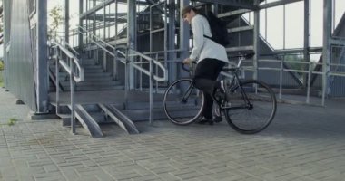 Bir adam merdivene bisikletle gider, bisikleti kollarına alır ve yukarı taşır.