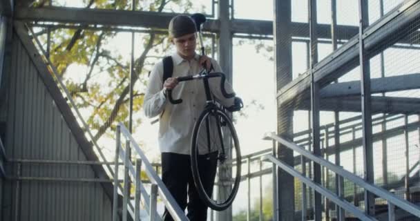 Un jeune homme porte une bicyclette vers le bas échelle, pendu sur son épaule — Video