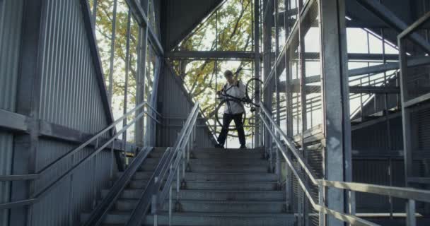 A young man carries a bicycle down ladder, hanged it on his shoulder — Stock Video