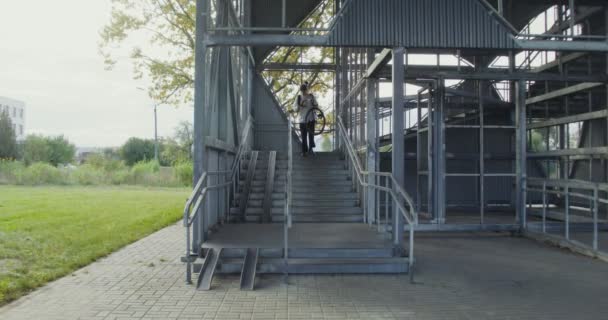 A young man carries a bicycle down a metal ladder — Stock Video