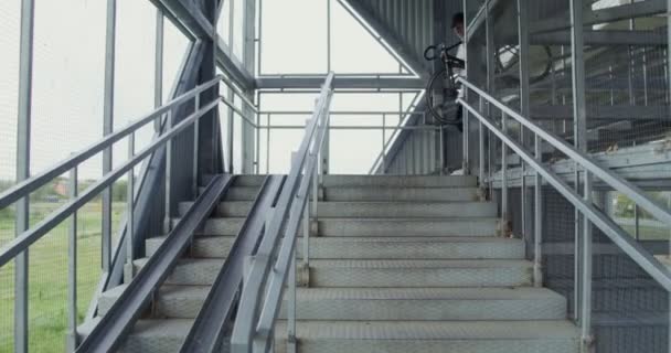 Ένας νεαρός κουβαλάει ένα ποδήλατο κάτω από μια μεταλλική σκάλα. — Αρχείο Βίντεο