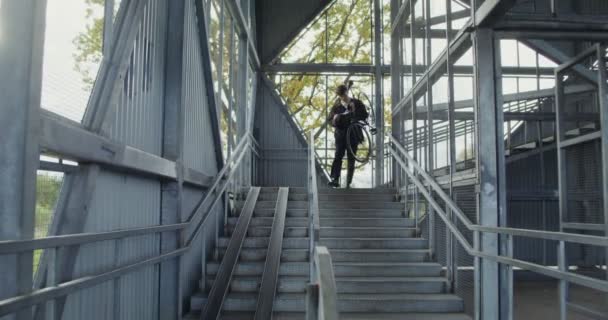 Genç bir adam metal bir merdivenden aşağı bisiklet taşıyor. — Stok video