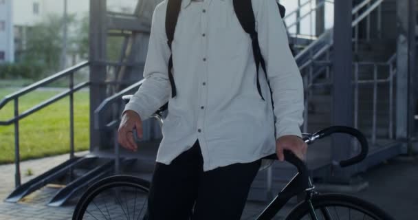 若い男がカメラを真剣に見て自転車にもたれている。 — ストック動画