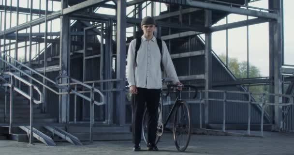 Un uomo tiene una bicicletta con la mano e guarda direttamente nella macchina fotografica — Video Stock