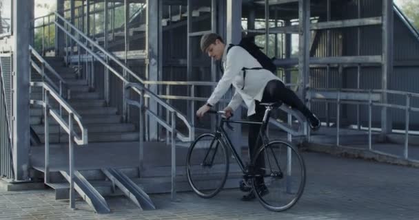 A man rides a bicycle to ladder, takes bicycle in his arms and carries it up — Stock Video