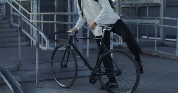 En man cyklar till stegen, tar cykeln i famnen och bär upp den. — Stockvideo