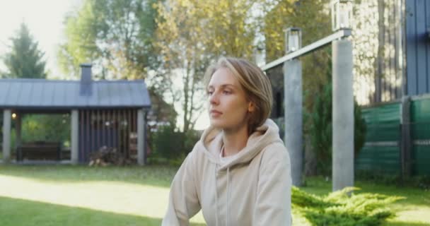 Een jonge vrouw in sportkleding doet oefeningen op het gazon in de buurt van een modern huisje — Stockvideo