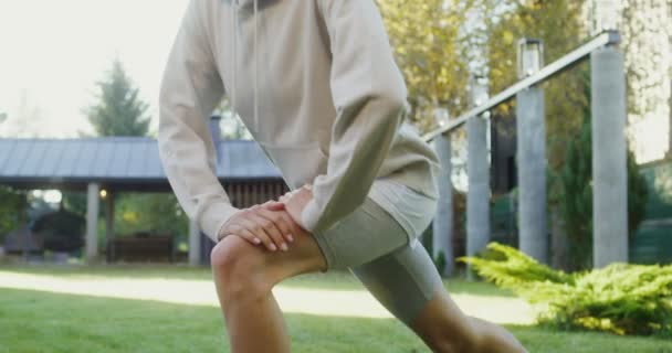 En ung kvinna i sportkläder tränar på gräsmattan nära en modern stuga — Stockvideo