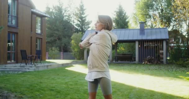 Młoda kobieta w odzieży sportowej ćwiczy na trawniku w pobliżu nowoczesnego domku — Wideo stockowe