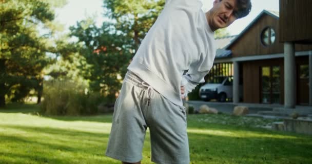 A young man in sportswear exercises in the fresh air near a modern mansion — Stock Video