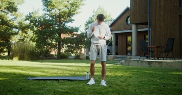 En ung man i sportkläder övningar i den friska luften nära en modern herrgård — Stockvideo