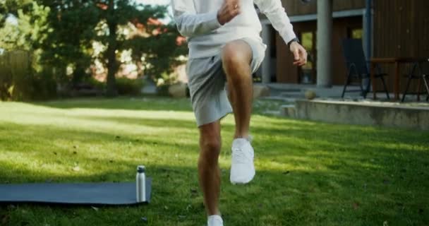 Um homem entra para esportes ao ar livre perto de uma casa de campo moderna, pulando no lugar — Vídeo de Stock