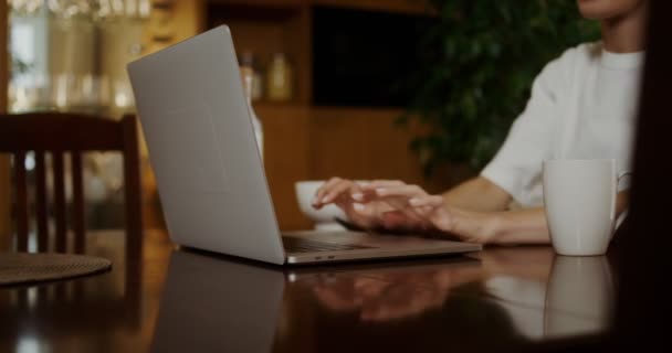 Молода жінка сідає за стіл, відкриває ноутбук і п'є каву — стокове відео
