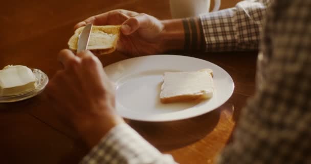 Jongeman strooit boter op toast, de voorbereiding voor het ontbijt in de moderne keuken — Stockvideo