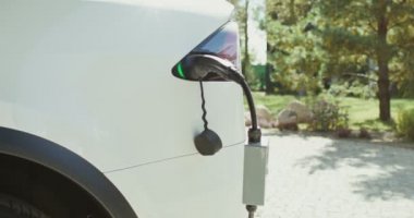 Arka bahçede şarj aletine bağlı elektrik kablosu olan elektrikli bir araba duruyor.