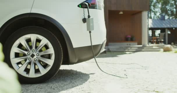 Электрический автомобиль с кабелем питания, подключенным к зарядному устройству, стоит на заднем дворе — стоковое видео