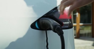 Bir adam elektrik kablosunu elektrikli arabadan ayırır ve kapağı kapatır.