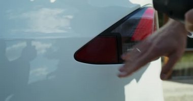 Genç bir adam elektrik kablosunu beyaz bir elektrikli arabaya bağlıyor.