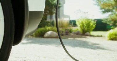 Arka bahçede şarj aletine bağlı elektrik kablosu olan elektrikli bir araba duruyor.