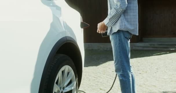 Μια νεαρή γυναίκα βγάζει ένα καλώδιο ρεύματος από ένα ηλεκτρικό αυτοκίνητο και φεύγει. — Αρχείο Βίντεο
