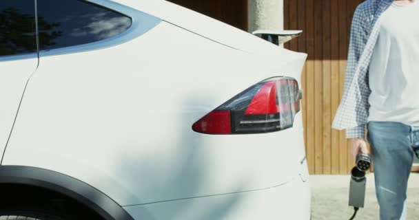 Mladý muž připojí napájecí kabel k bílému elektrickému autu — Stock video