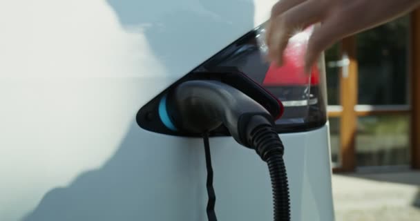 Mies irrottaa sähkökaapelin sähköautosta ja sulkee luukun. — kuvapankkivideo