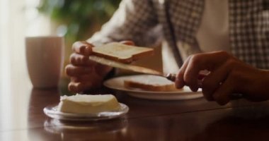 Genç adam tostun üzerine tereyağı sürüyor, modern mutfakta kahvaltıya hazırlanıyor.