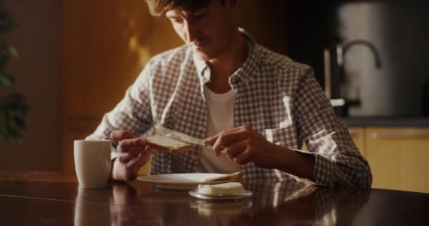 Mladý muž namaže máslo na toast a připraví snídani v moderní kuchyni — Stock video