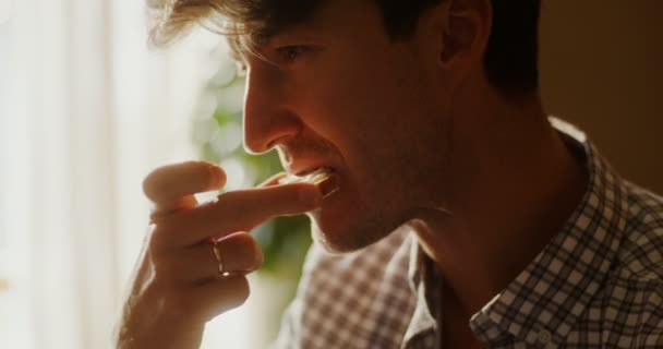 Młody człowiek je tosty z masłem i zmywa je kawą, jedząc śniadanie — Wideo stockowe