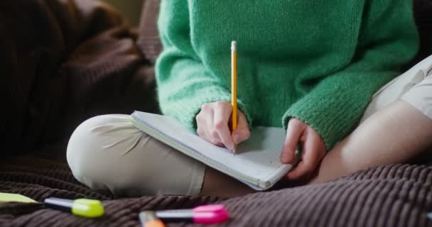 Das Mädchen macht sich Notizen in einem Notizbuch, das auf der Couch sitzt, in Großaufnahme — Stockvideo