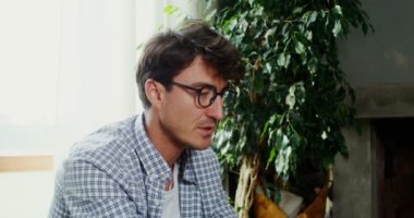 Modern bir iç mekanda koltukta oturan bir adam bilgisayarla görüntülü konuşma yapar.