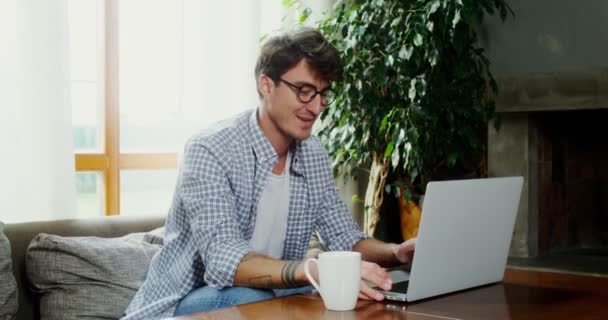 Чоловік розмовляє відеочатом на ноутбуці, сидячи на дивані в сучасному інтер'єрі — стокове відео
