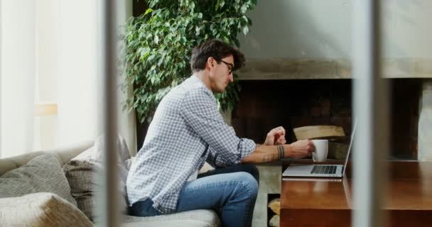 Mężczyzna korzysta z laptopa siedząc na kanapie przy stoliku w nowoczesnym wnętrzu — Wideo stockowe