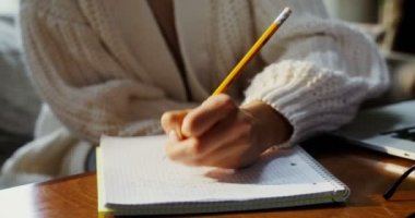 Not defterine sol eliyle not alan bir kadın açık dizüstü bilgisayarın yanında oturuyor.