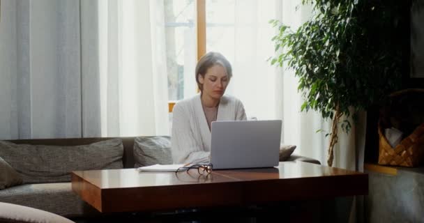 Egy nő laptopot használ, és jegyzetel egy jegyzetfüzetben a bal kezével. — Stock videók