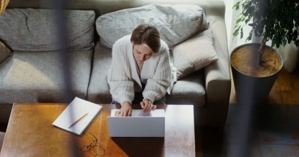 Jovem mulher digitando em um laptop, sentado em um sofá em um interior de casa — Vídeo de Stock