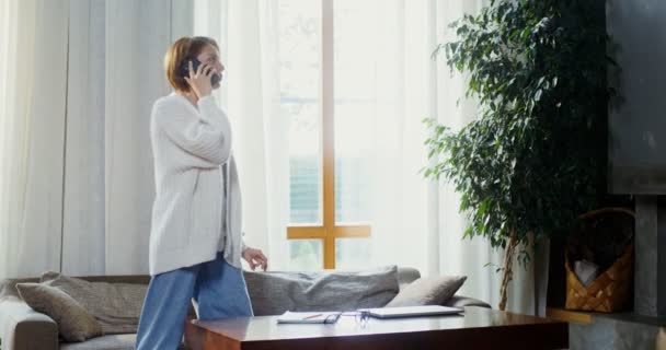 Genç bir kadın odada yürürken telefonla konuşuyor. — Stok video